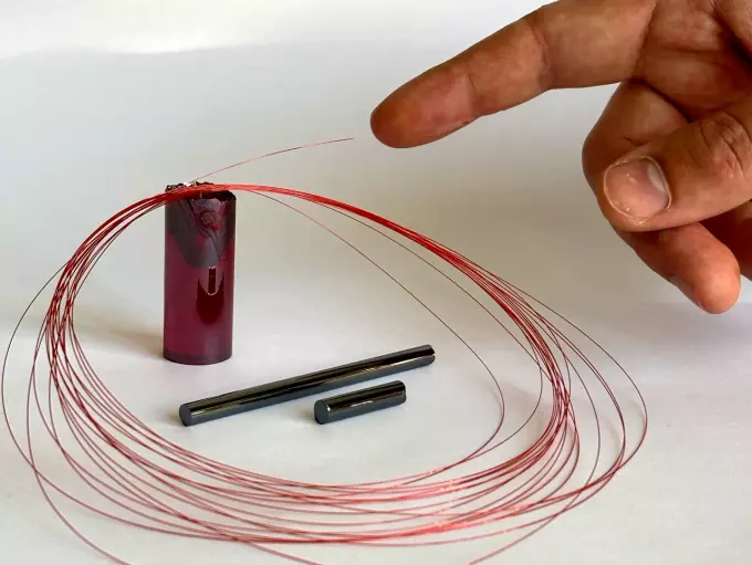 Волоконный световод с сердцевиной, обогащенной ионами празеодима, в масштабе руки. Показаны заготовки стекол для вытяжки волоконного световода: красное — оболочечное сульфидное стекло, темное — сердцевинное селенидное стекло, обогащенное празеодимом